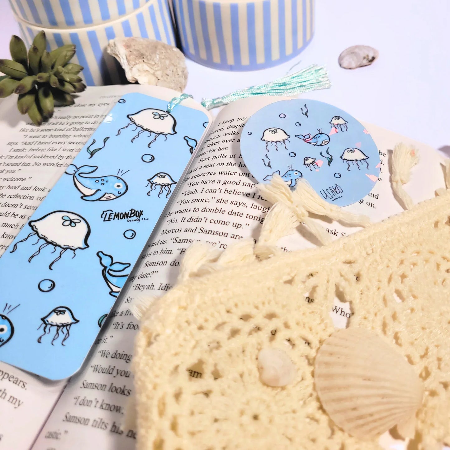 Bookmark with cartoon designs on a book, surrounded by seashells and a small plant.