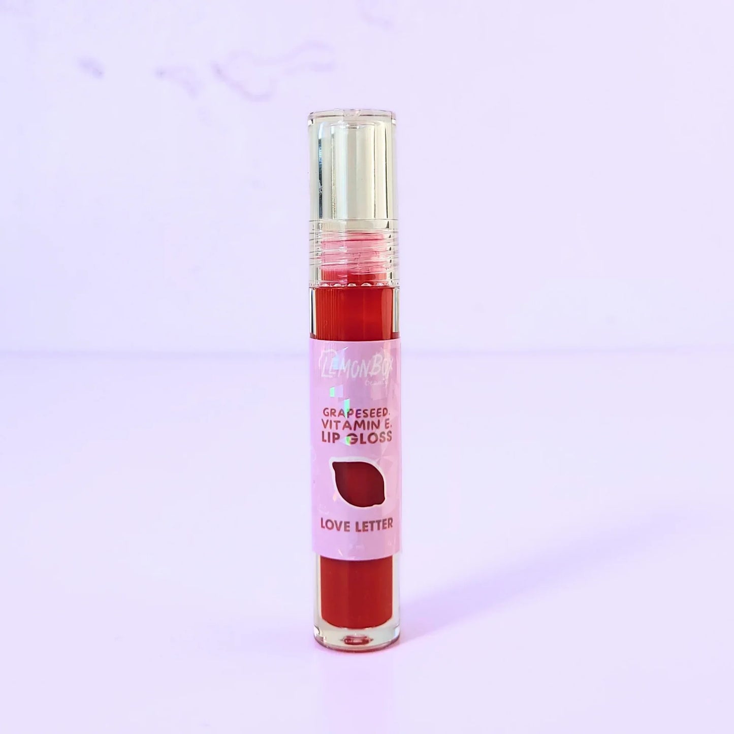 Lemon Box Beauty Grapeseed Vitamin E Lip Gloss in shade Love Letter - vibrant classic red hydrating lip oil in a clear tube against a lavender background.