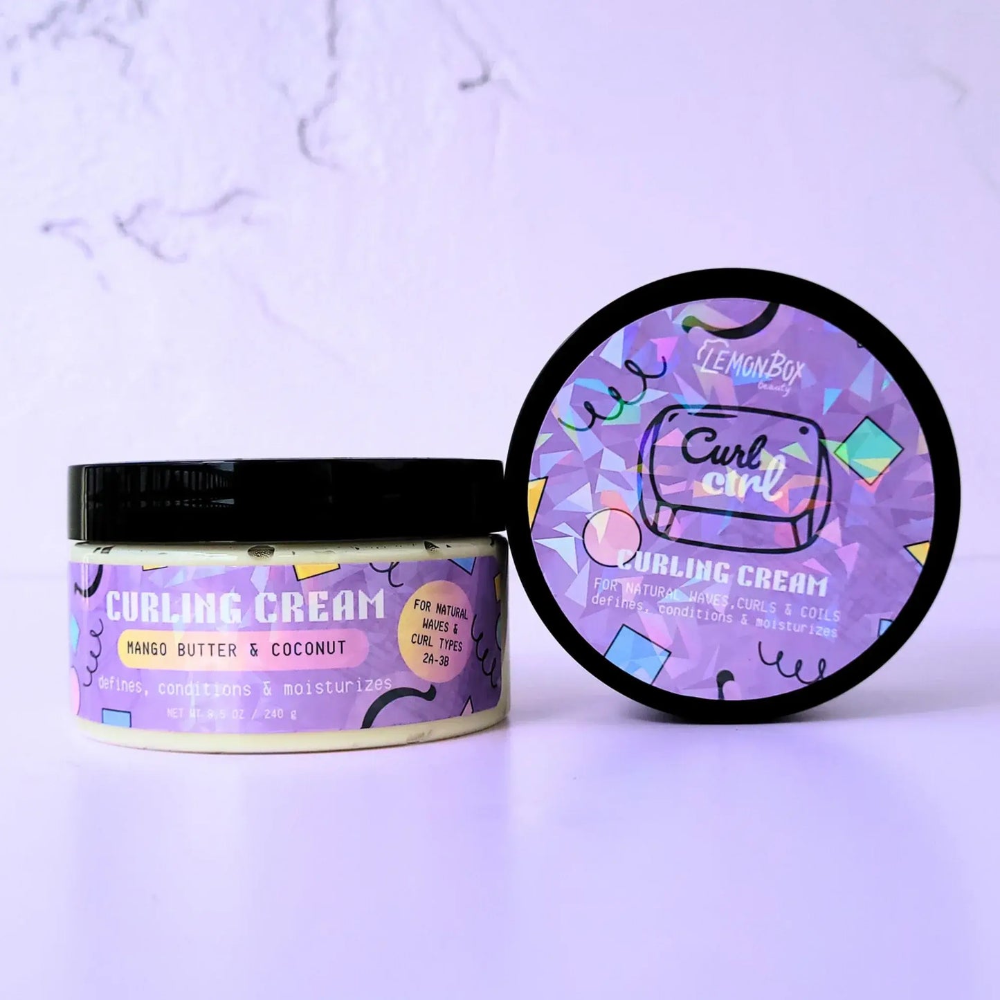 An 8.5 oz jar of LemonBox Beauty Curling Cream featuring Mango Butter and Coconut, with a purple geometric label and a black lid, set against a soft lavender background.