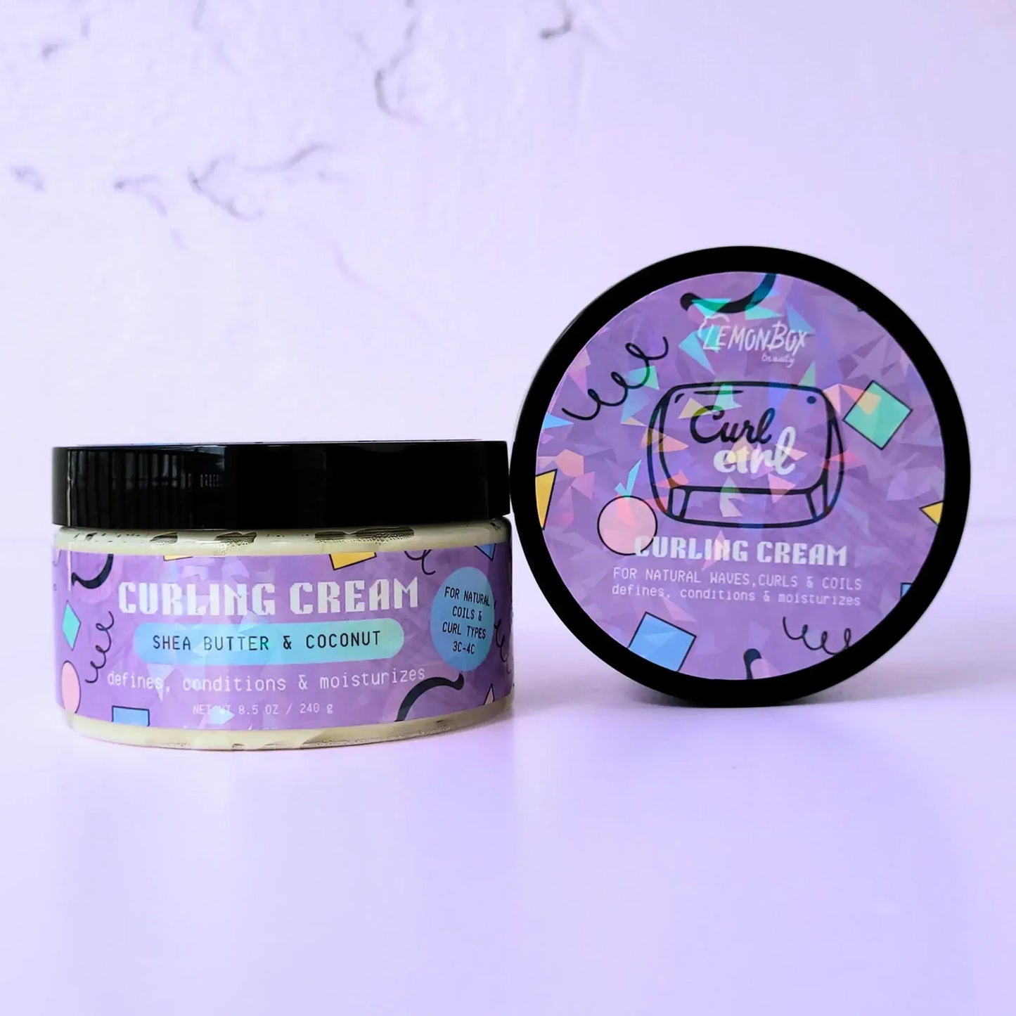 An 8.5 oz jar of LemonBox Beauty Curling Cream featuring Shea Butter and Coconut, with a blue and purple geometric label and a black lid, set against a soft lavender background.