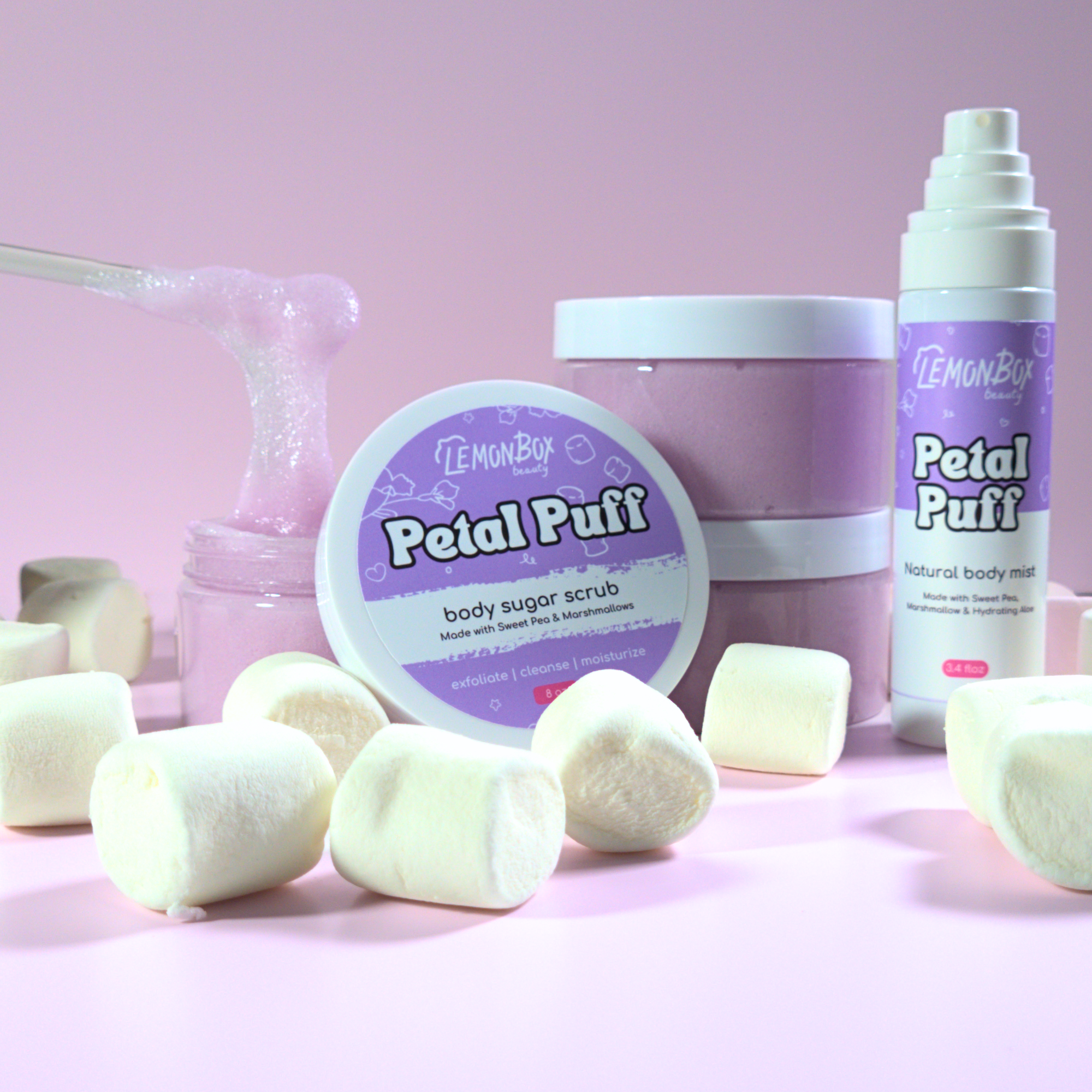 Lemon Box Petal Puff products including a jar, bottle, and body scrub on a pink background with marshmallows.