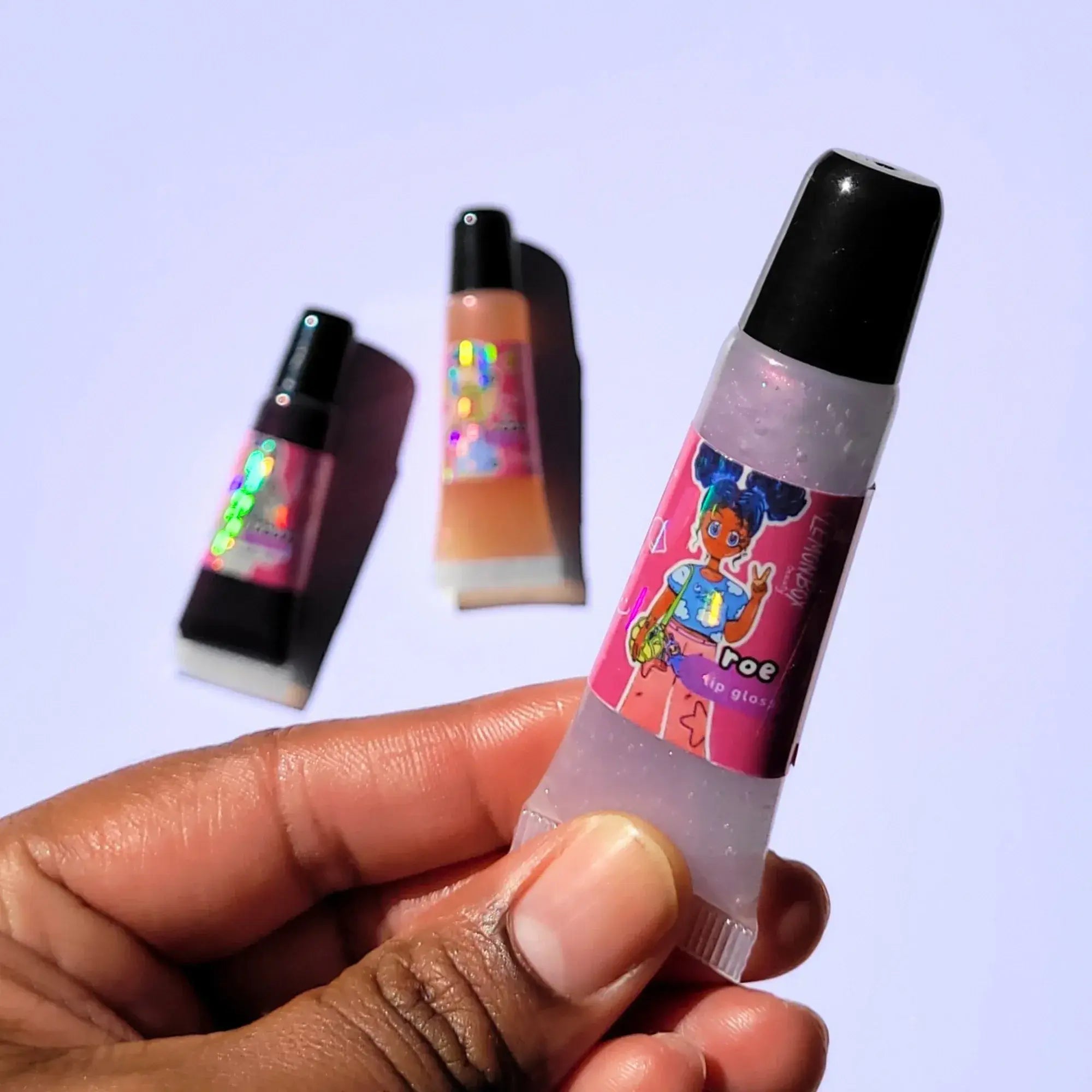 Lemon Box Beauty Roe Anime Shine Lip Gloss - translucent iridescent purple vegan lip oil in a squeeze tube with custom anime character artwork of a girl with blue space buns.