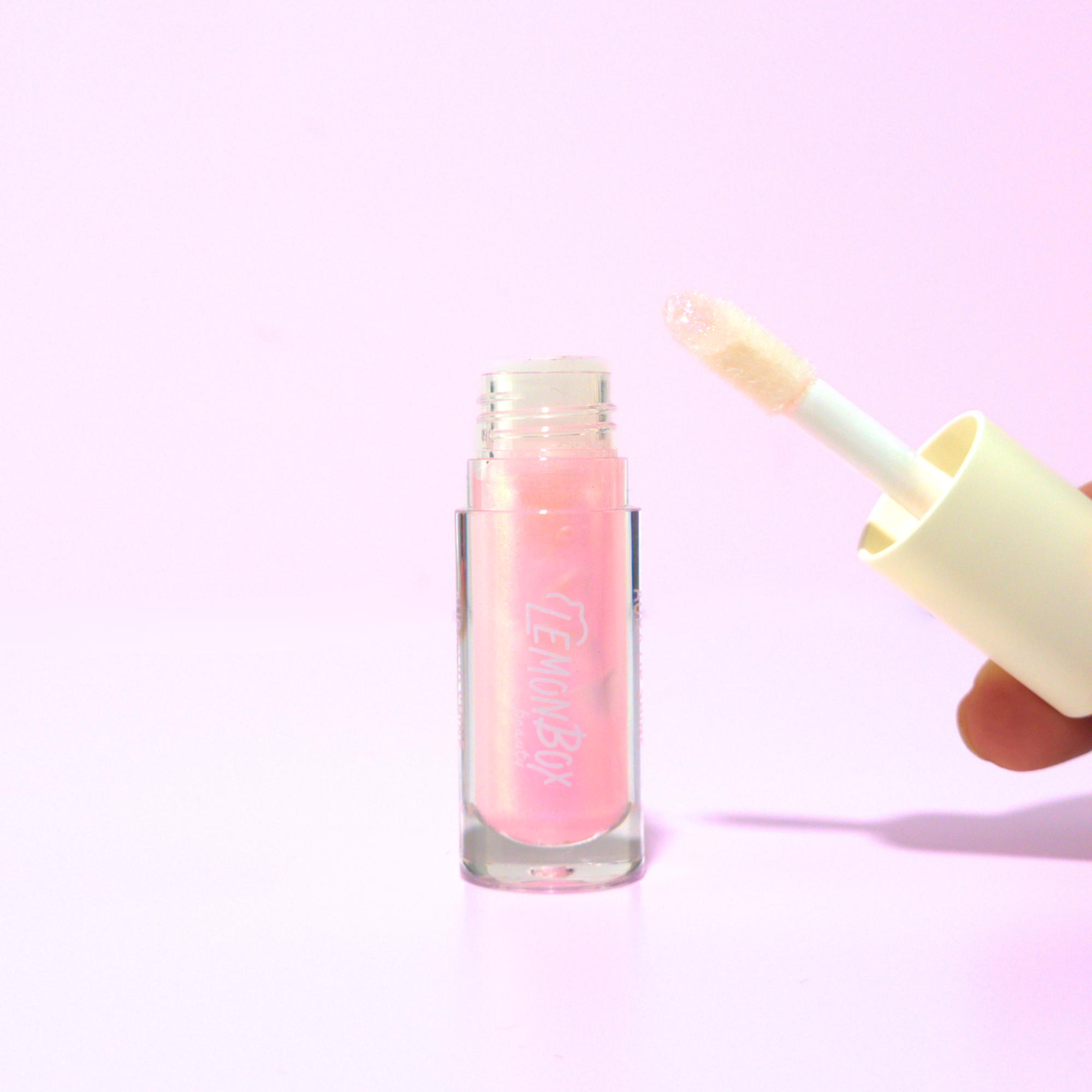 Pink lip gloss with applicator on a light purple background