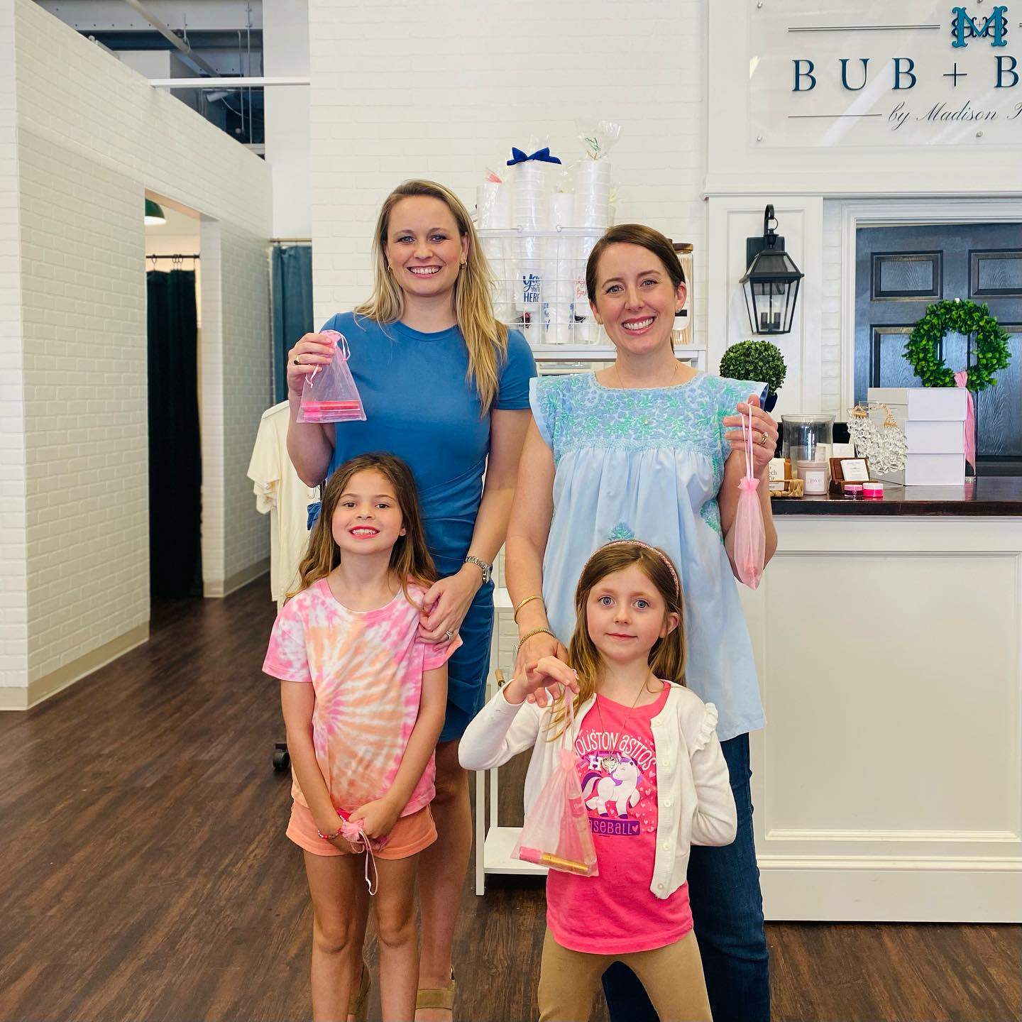 Two women and two young girls holding pink bottles in a store setting with 'BUB + B' branding.