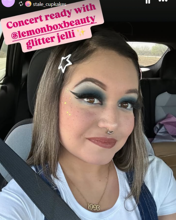 Person in a car with makeup and glitter effects, sitting in the back seat.