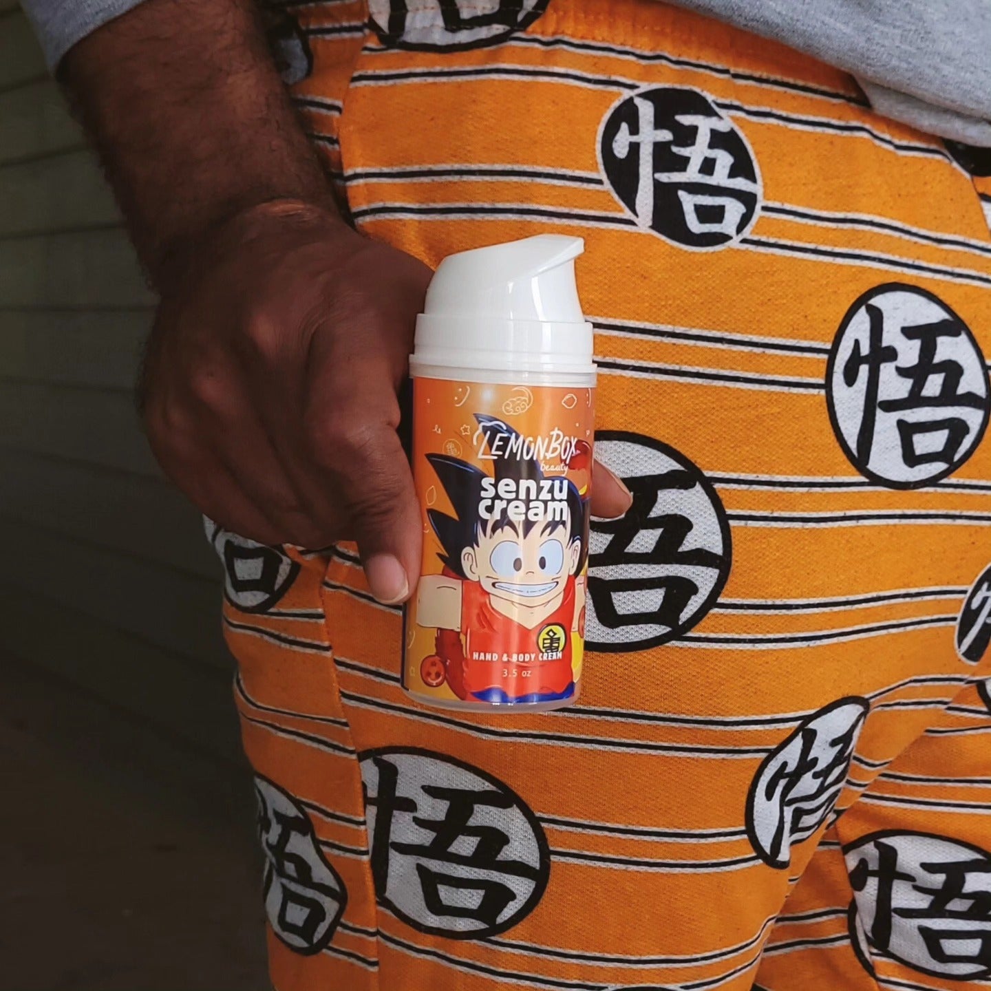 Person holding a container of senzu cream with orange pants featuring black symbols dragon ball