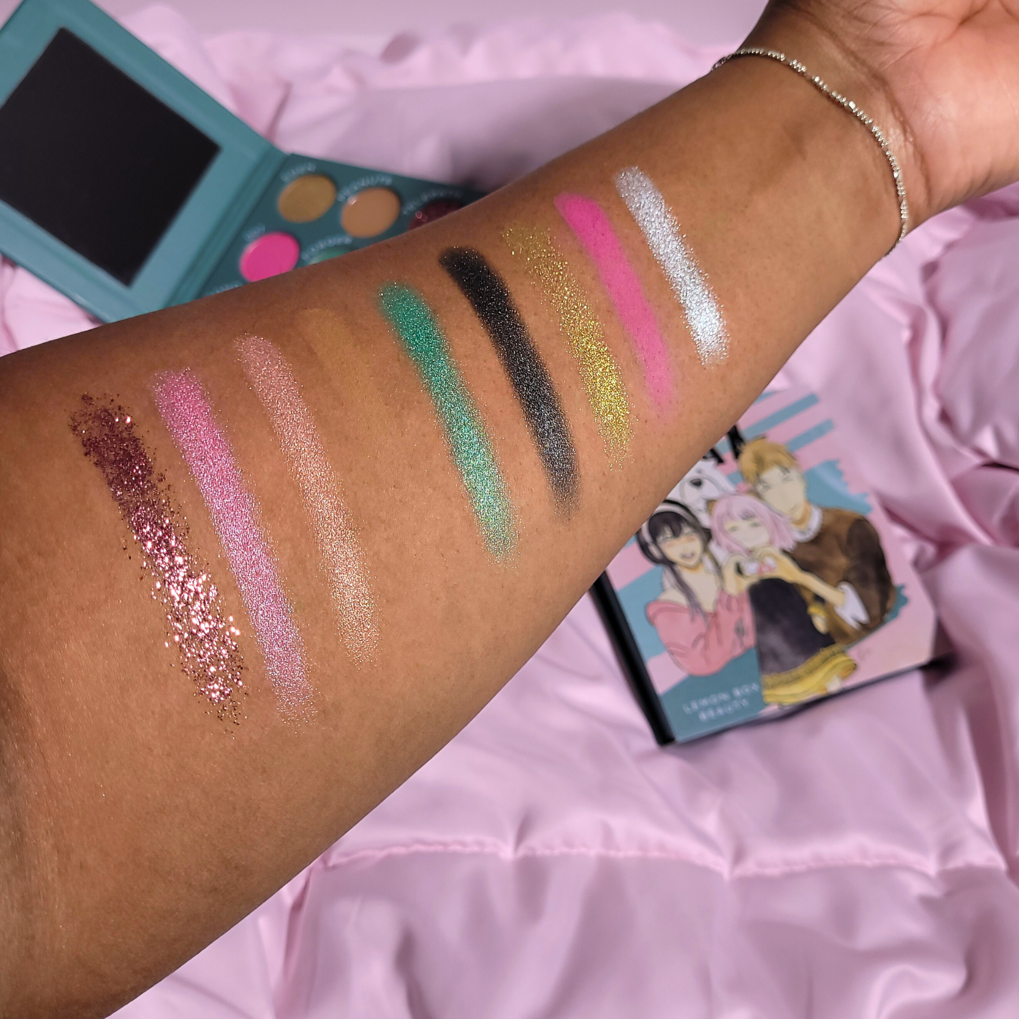 Makeup swatches on a person's arm with a pink background