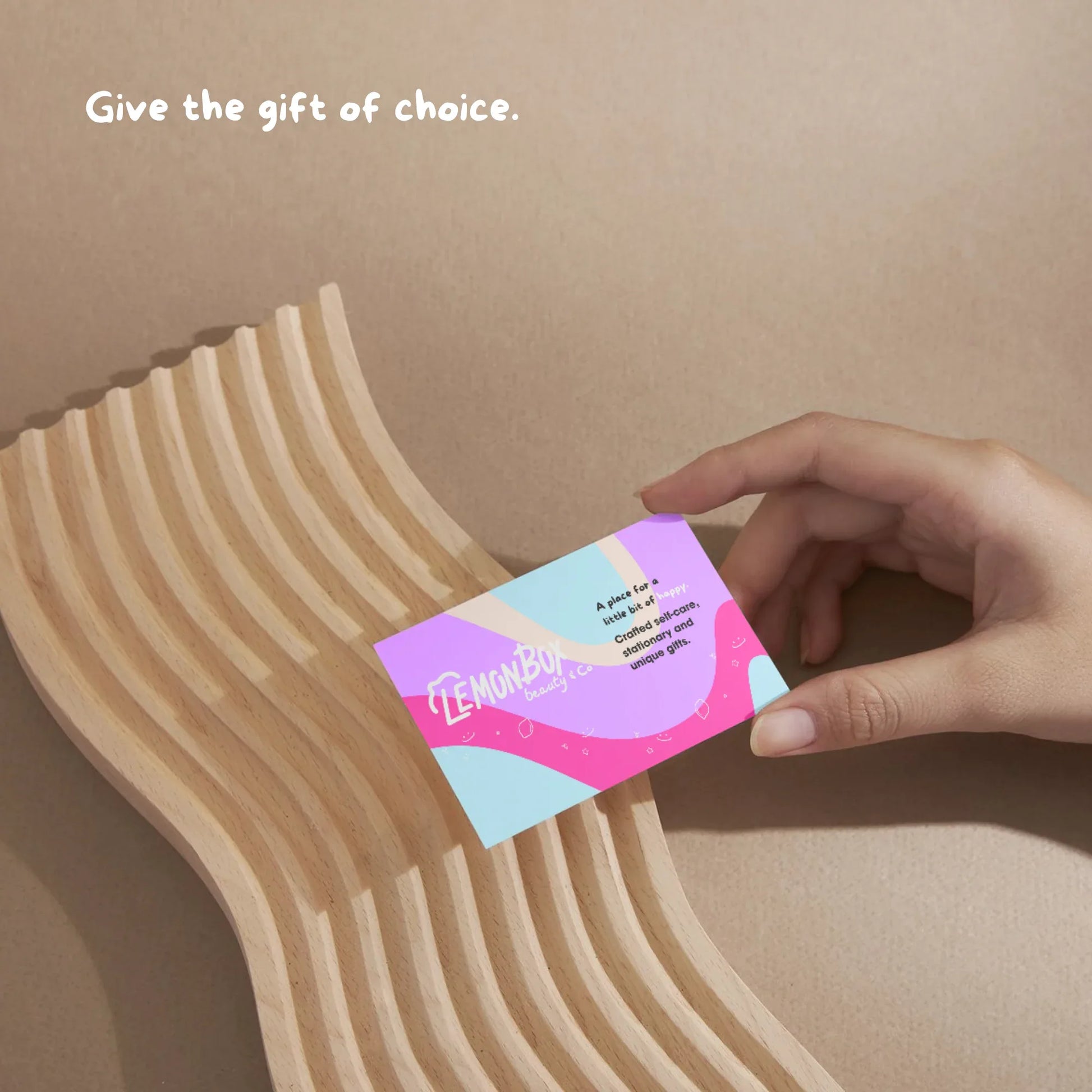 Hand holding a colorful card with 'Lemonade' branding against a beige background.