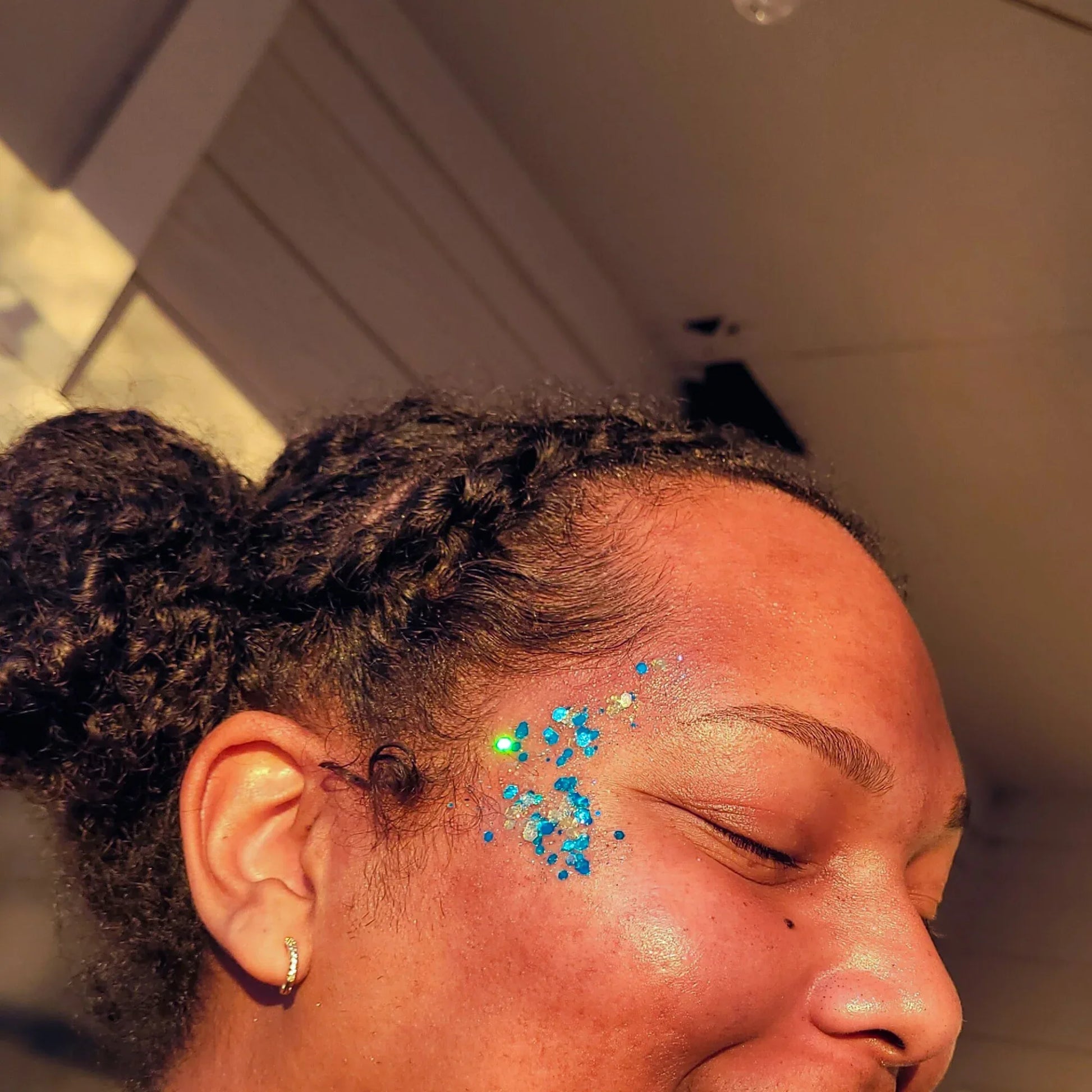 Model wearing Lemon Box Beauty Teal Tails and Frosted Glitter Jelli—vibrant teal and iridescent silver chunky body glitter applied to the temple and cheekbone area.