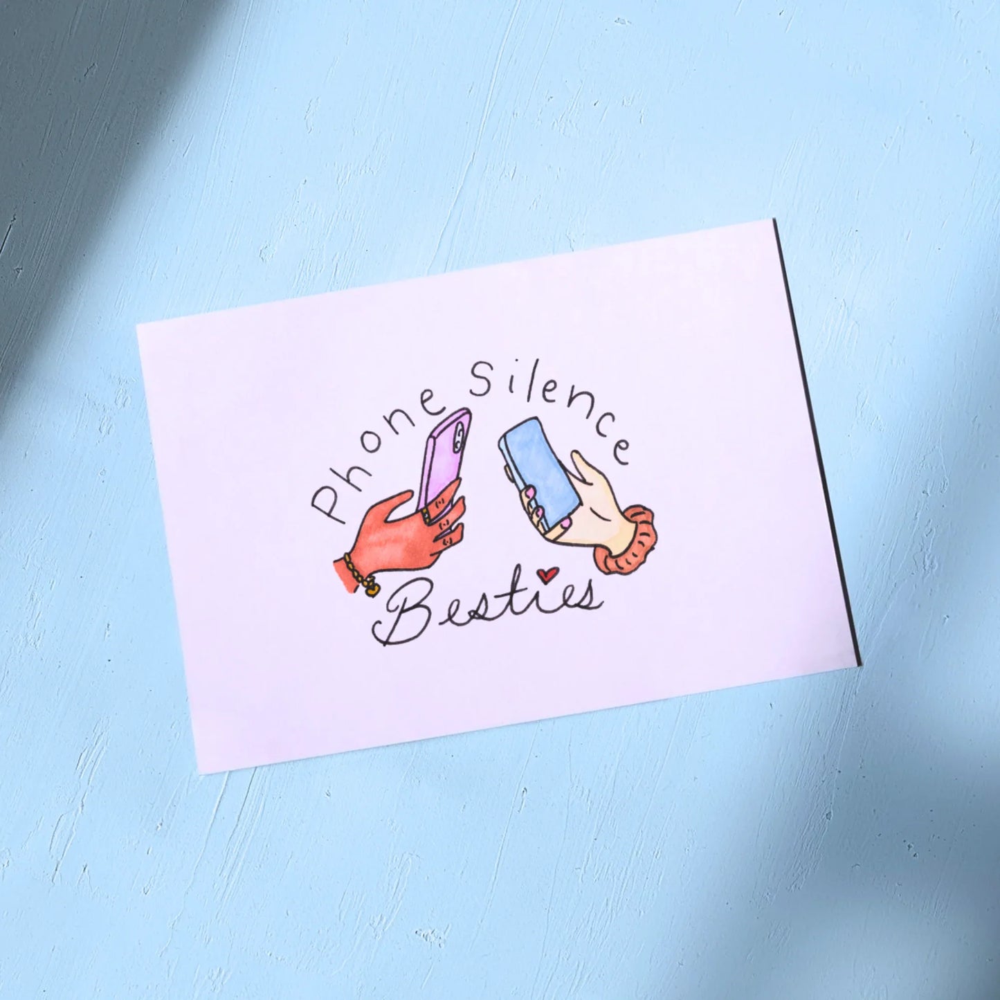 White Greeting Card with illustration of two hands holding phones and text 'Phone Silence Besties' on a light blue background