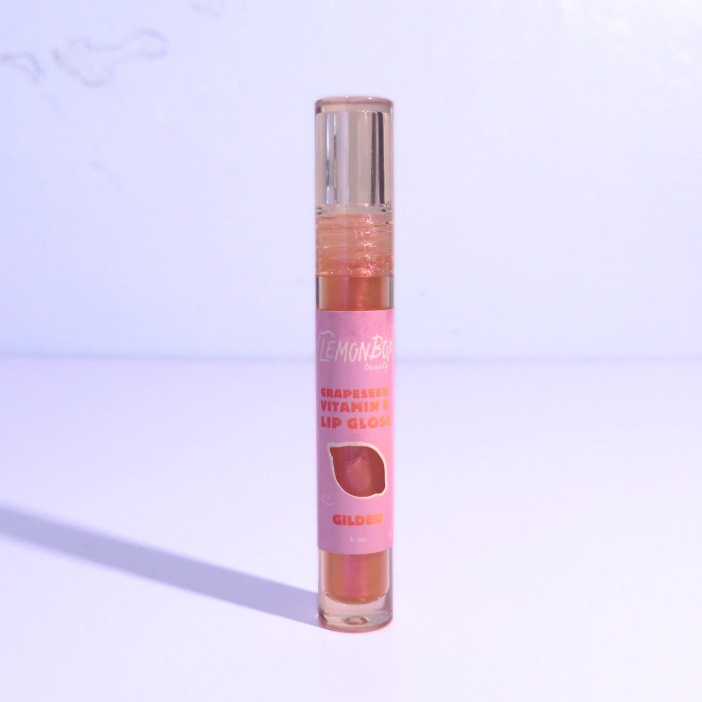 Lip gloss with bronze shade on a light purple background
