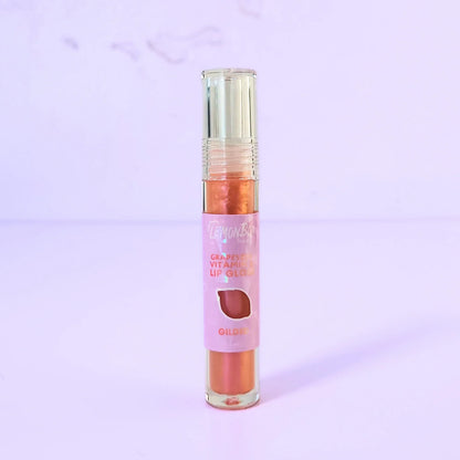 Lemon Box Beauty Grapeseed Vitamin E Lip Gloss in shade Gilded - shimmering copper-gold hydrating lip oil in a clear tube against a lavender background.