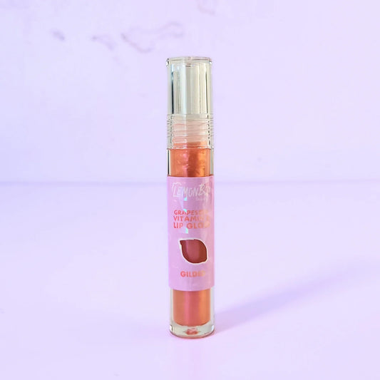 Lemon Box Beauty Grapeseed Vitamin E Lip Gloss in shade Gilded - shimmering copper-gold hydrating lip oil in a clear tube against a lavender background.