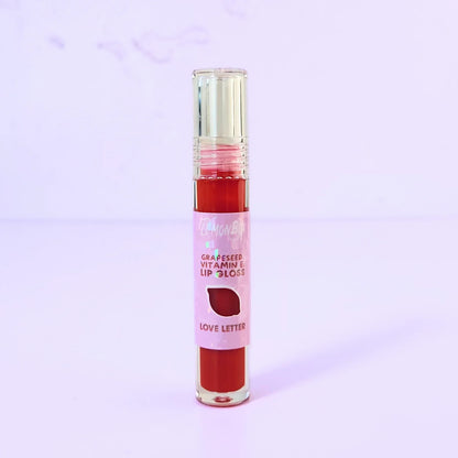 Lemon Box Beauty Grapeseed Vitamin E Lip Gloss in shade Love Letter - vibrant classic red hydrating lip oil in a clear tube against a lavender background.
