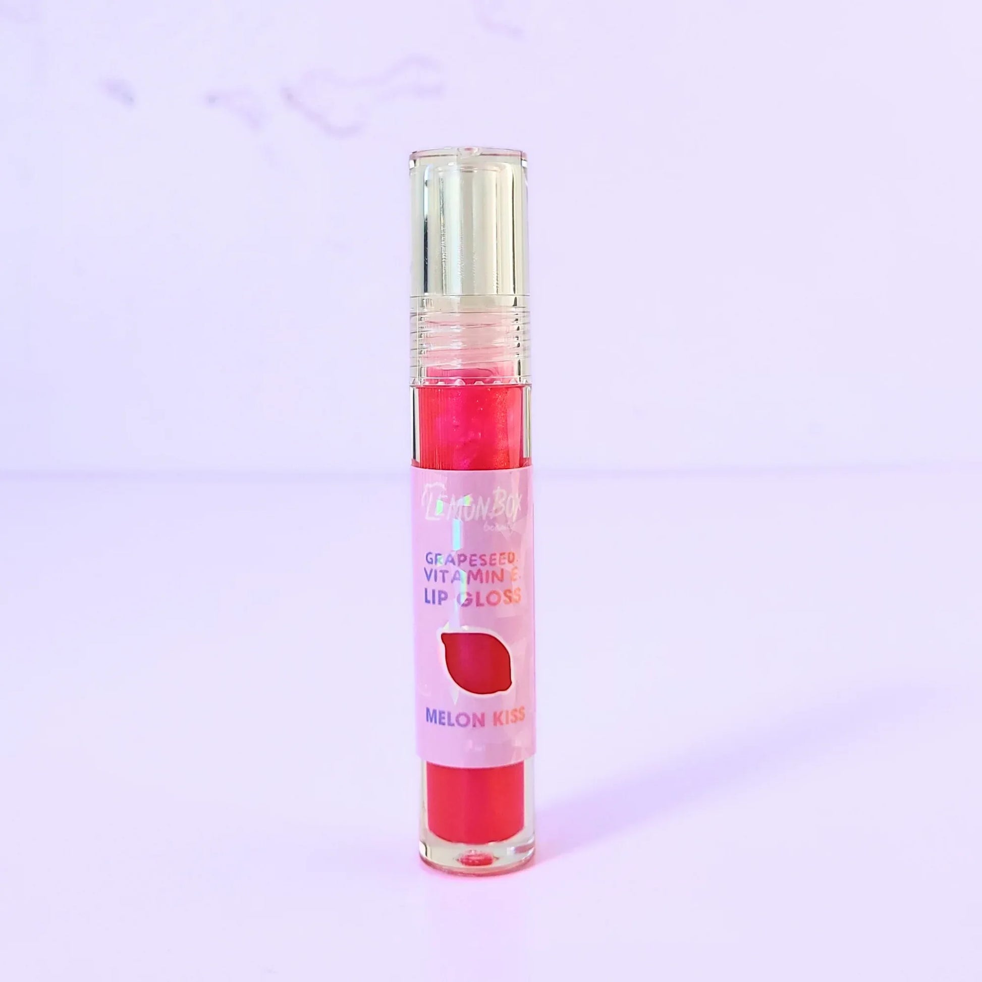 Lemon Box Beauty Grapeseed Vitamin E Lip Gloss in shade Melon Kiss - shimmering hot pink hydrating lip oil in a clear tube against a lavender background.