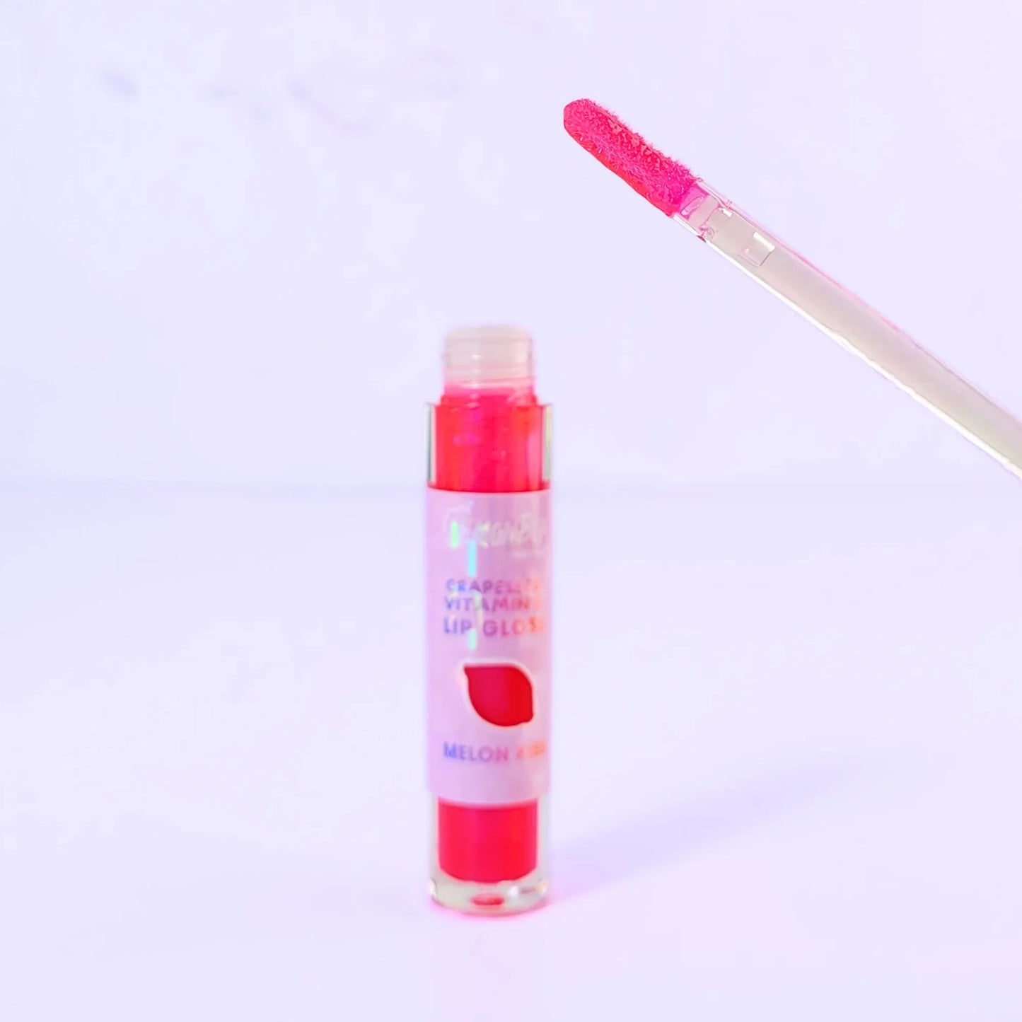 Lemon Box Beauty Grapeseed Vitamin E Lip Gloss in shade Melon Kiss - shimmering hot pink hydrating lip oil in a clear tube against a lavender background.