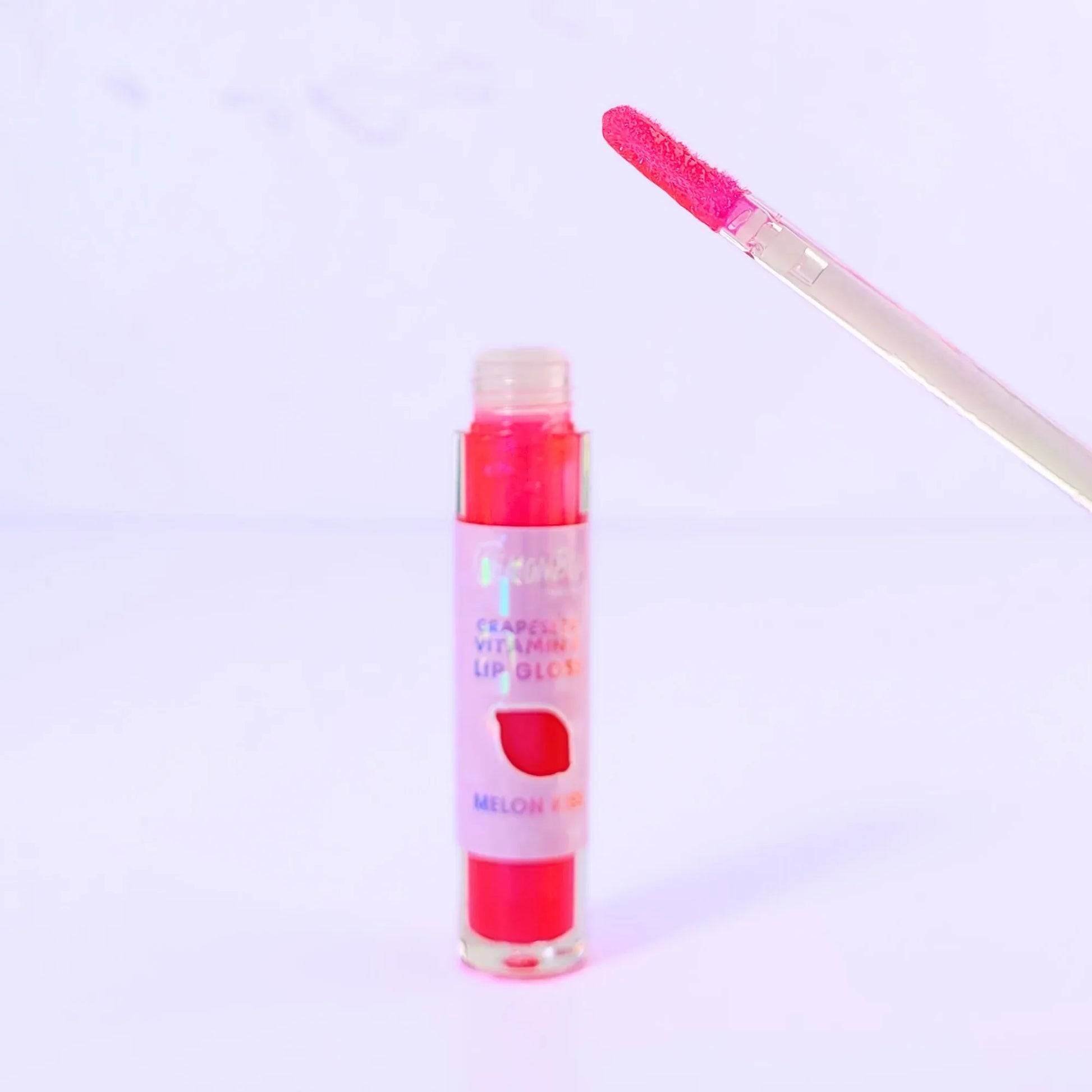 Lemon Box Beauty Grapeseed Vitamin E Lip Gloss in shade Melon Kiss - shimmering hot pink hydrating lip oil in a clear tube against a lavender background.