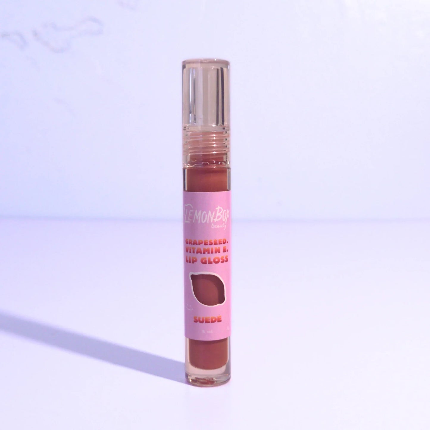Lip gloss with brown shade on a light purple background