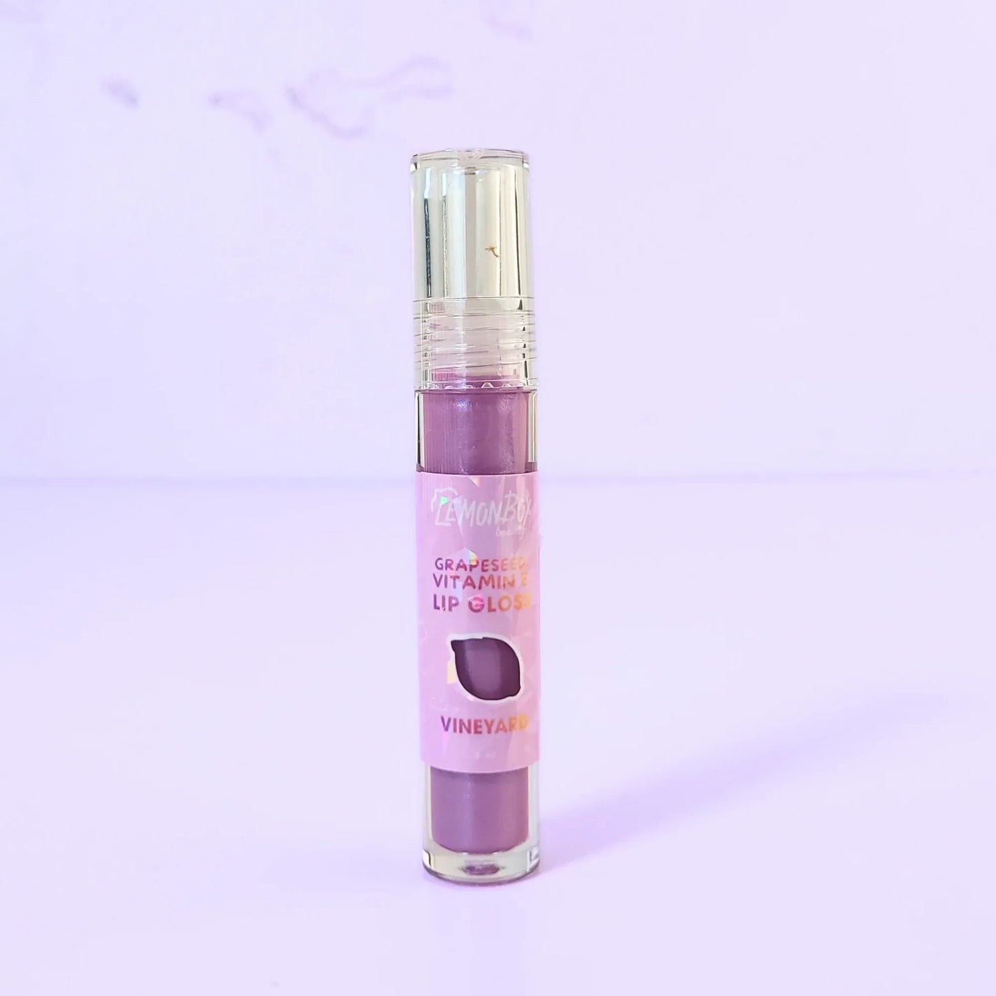 Lemon Box Beauty Grapeseed Vitamin E Lip Gloss in shade Vineyard - deep berry-plum hydrating lip oil in a clear tube against a lavender background.