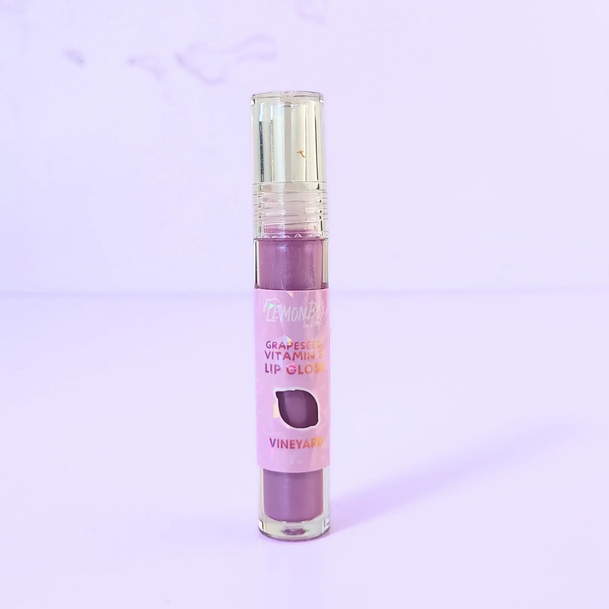 Lemon Box Beauty Grapeseed Vitamin E Lip Gloss in shade Vineyard - deep berry-plum hydrating lip oil in a clear tube against a lavender background.