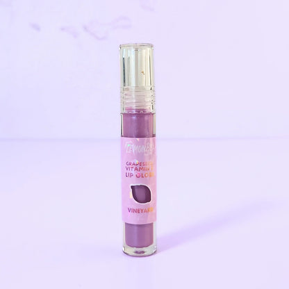 Lemon Box Beauty Grapeseed Vitamin E Lip Gloss in shade Vineyard - deep berry-plum hydrating lip oil in a clear tube against a lavender background.