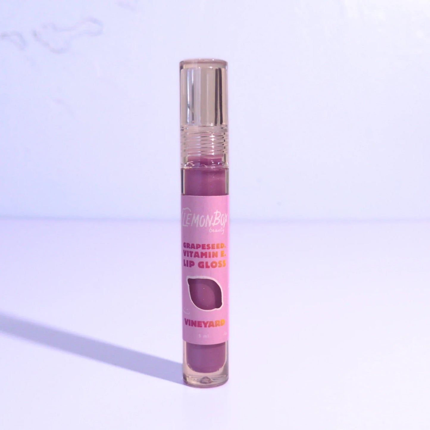 Lip gloss with a purple shade on a light purple background