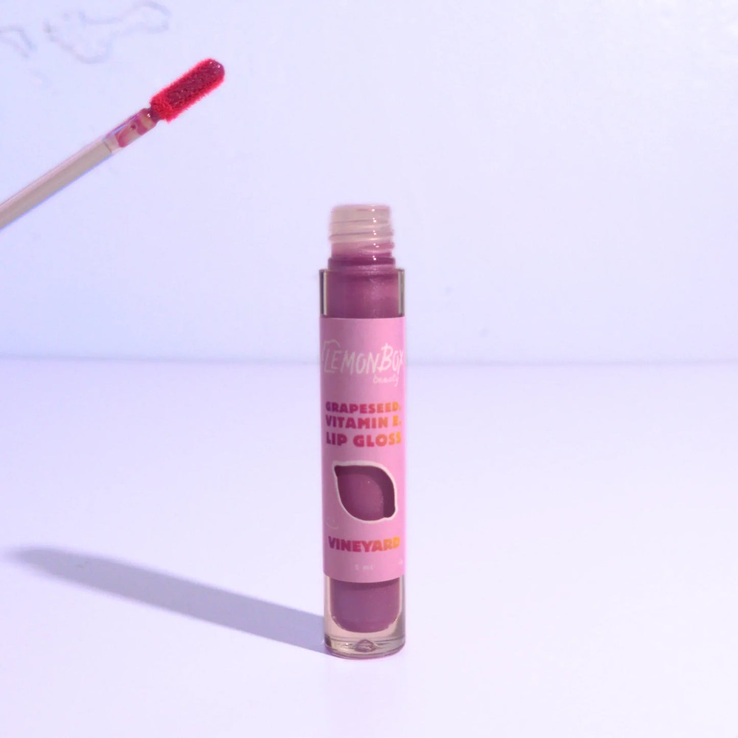 Lip gloss with wand applicator and purple body on a light purple background