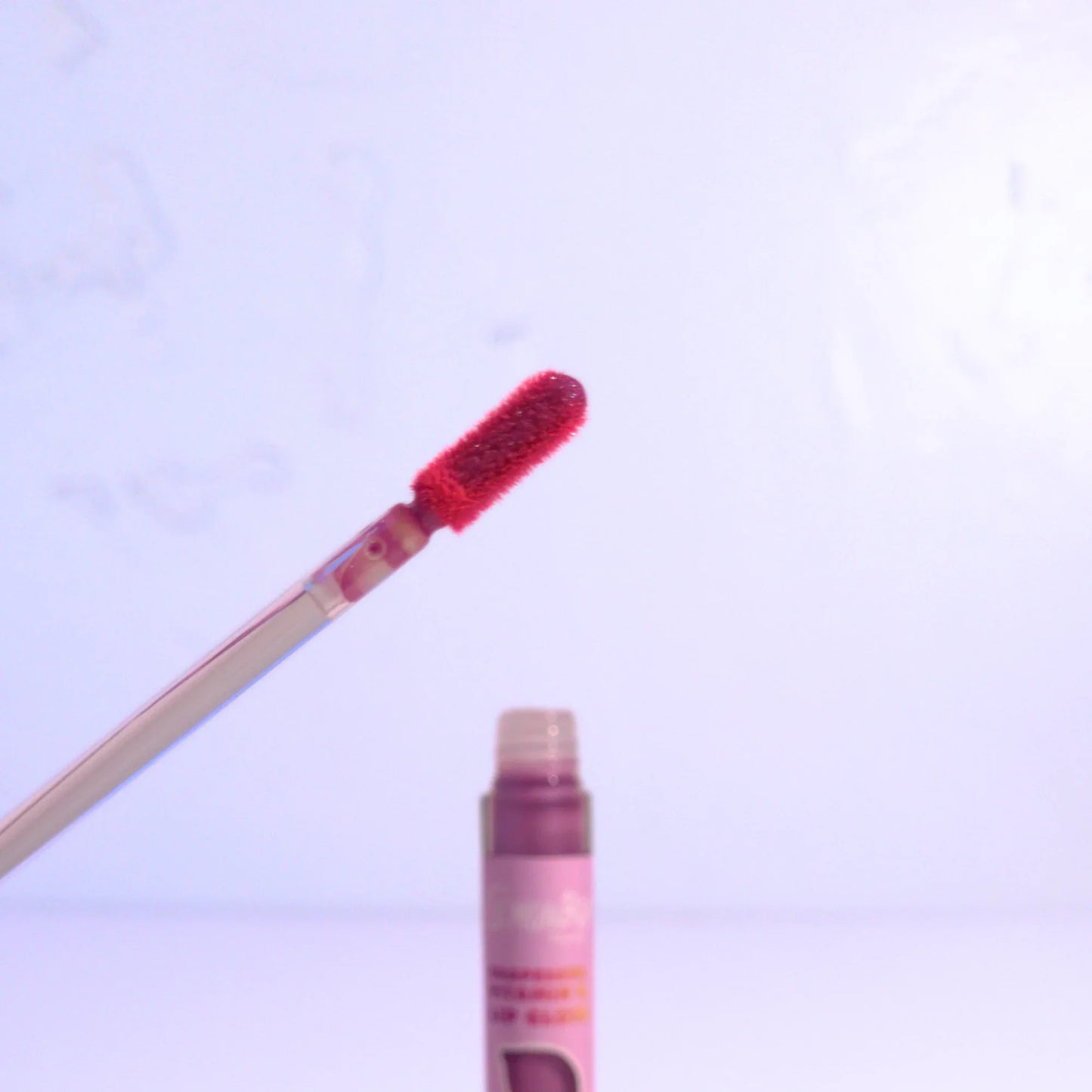 Lip gloss with wand applicator on a light purple background