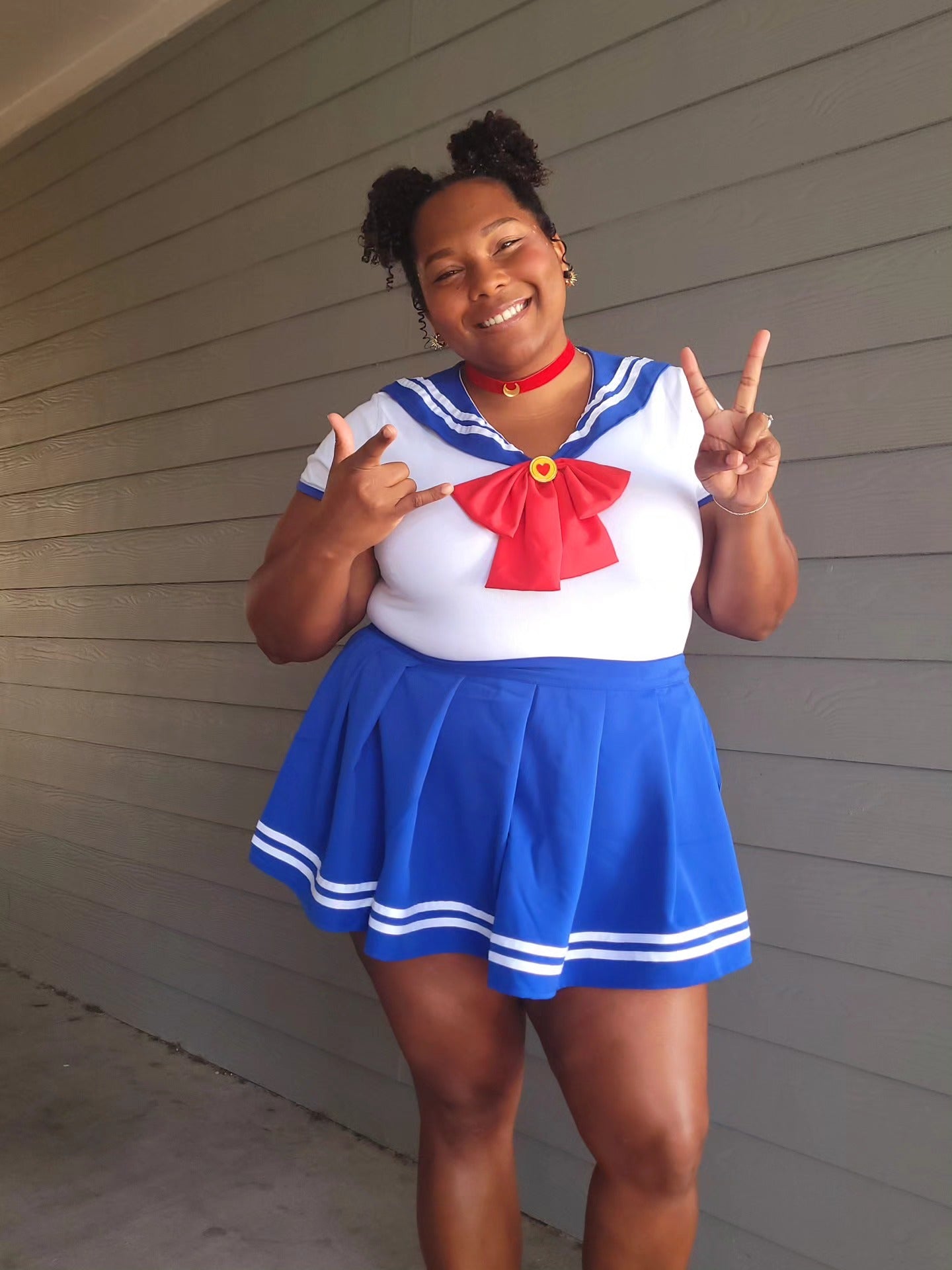 Person wearing a Sailor Moon costume, making peace signs in front of a gray wall.