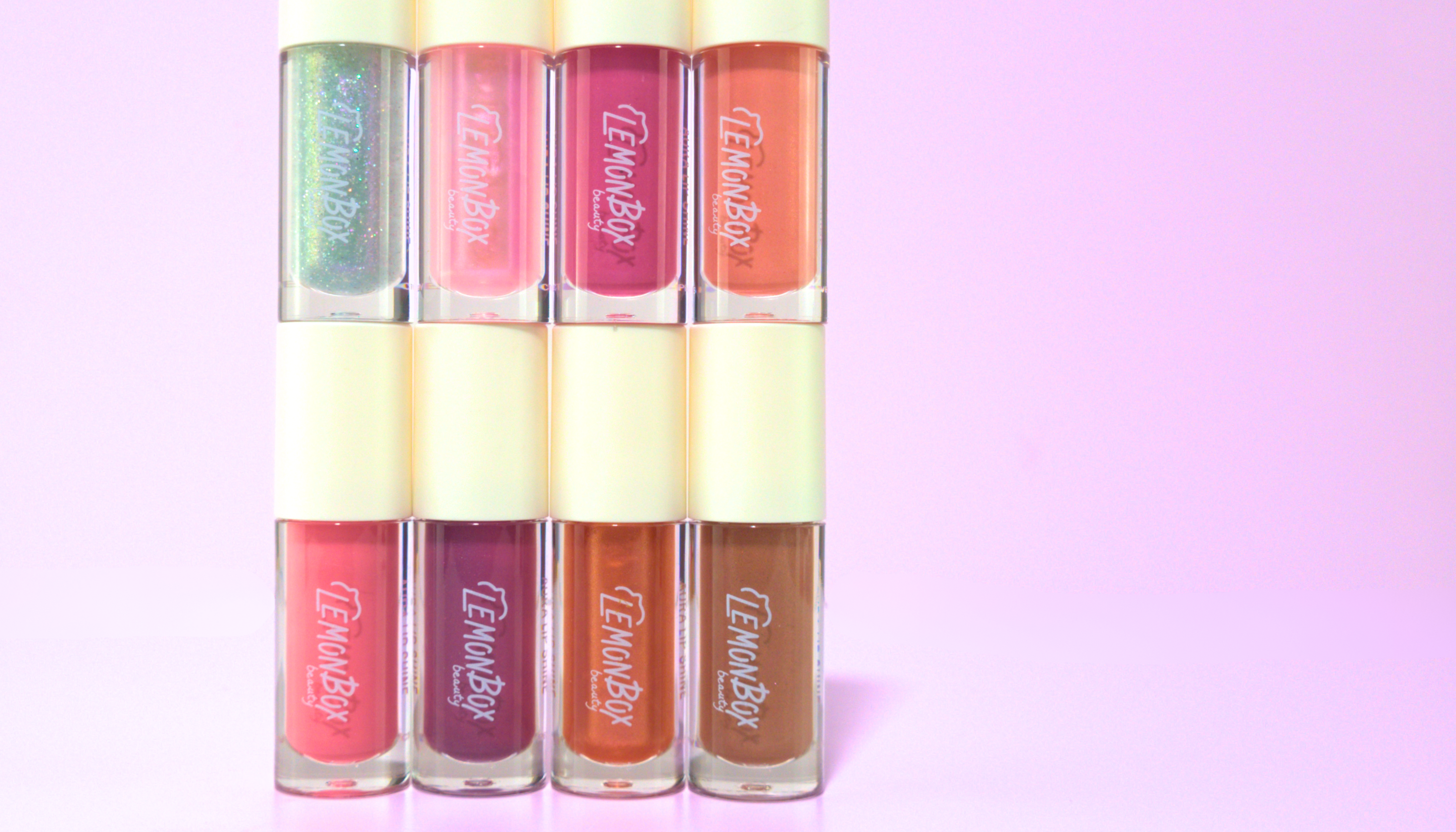 Set of six lip glosses with 'Lemon Bar' branding on a gradient pink background