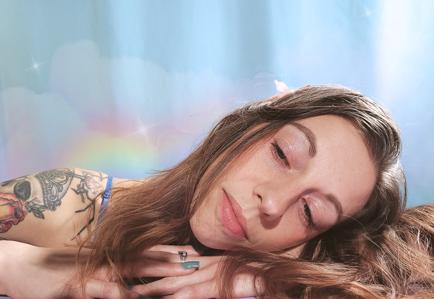 Woman with tattoos lying down against a light blue background with a rainbow.