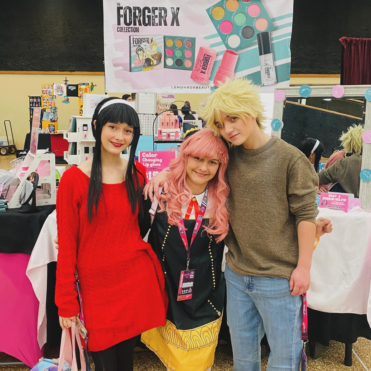 Three people with colorful hairstyles posing in front of a 'FORGER X' display at an event.