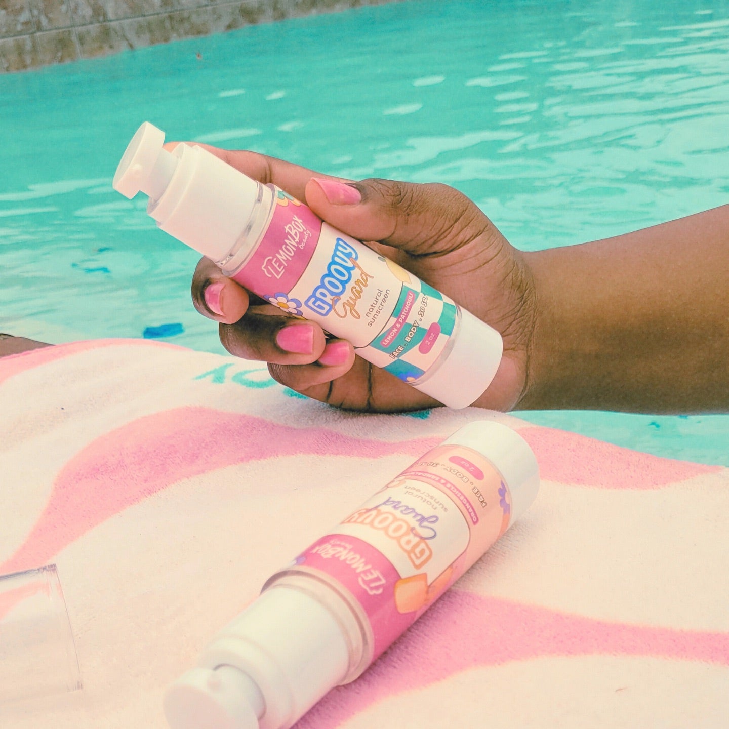 Hand holding a bottle of sunscreen with a pool in the background, Natural sunscreen
