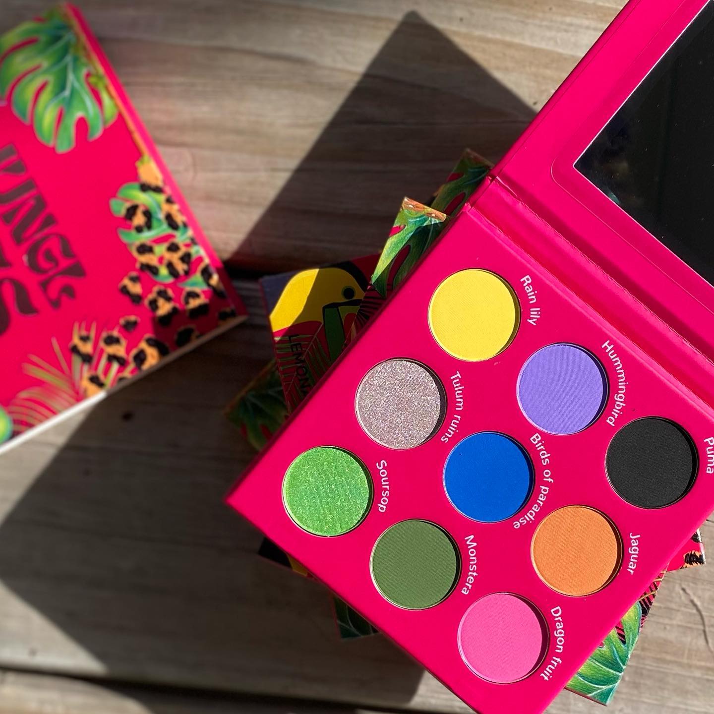 Pink makeup palette with colorful swatches on a wooden surface