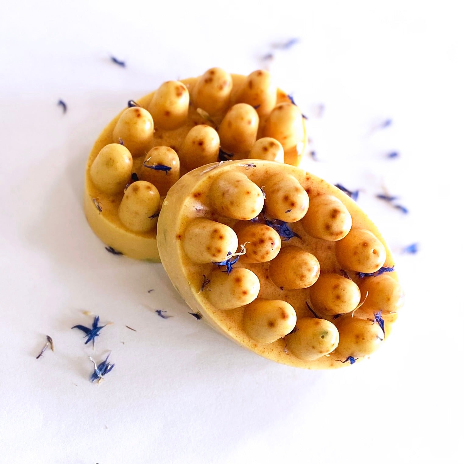 Two yellow soap bars with bubble texture on a white background with lavender flowers. Mango Tumeric
