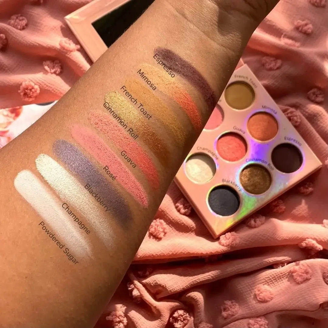 Makeup palette with swatches on a hand against a textured pink background
