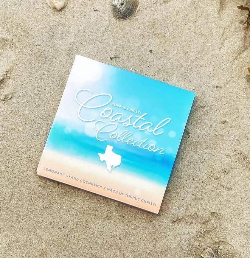 Cosmetic palette with 'Coastal Collection' branding on a sandy surface