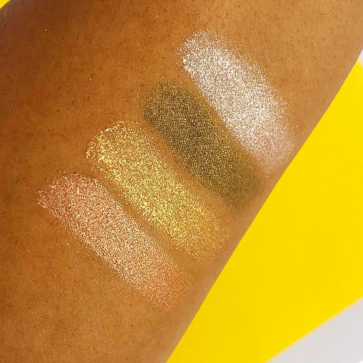 Close-up of three glittery makeup swatches on skin with a yellow background