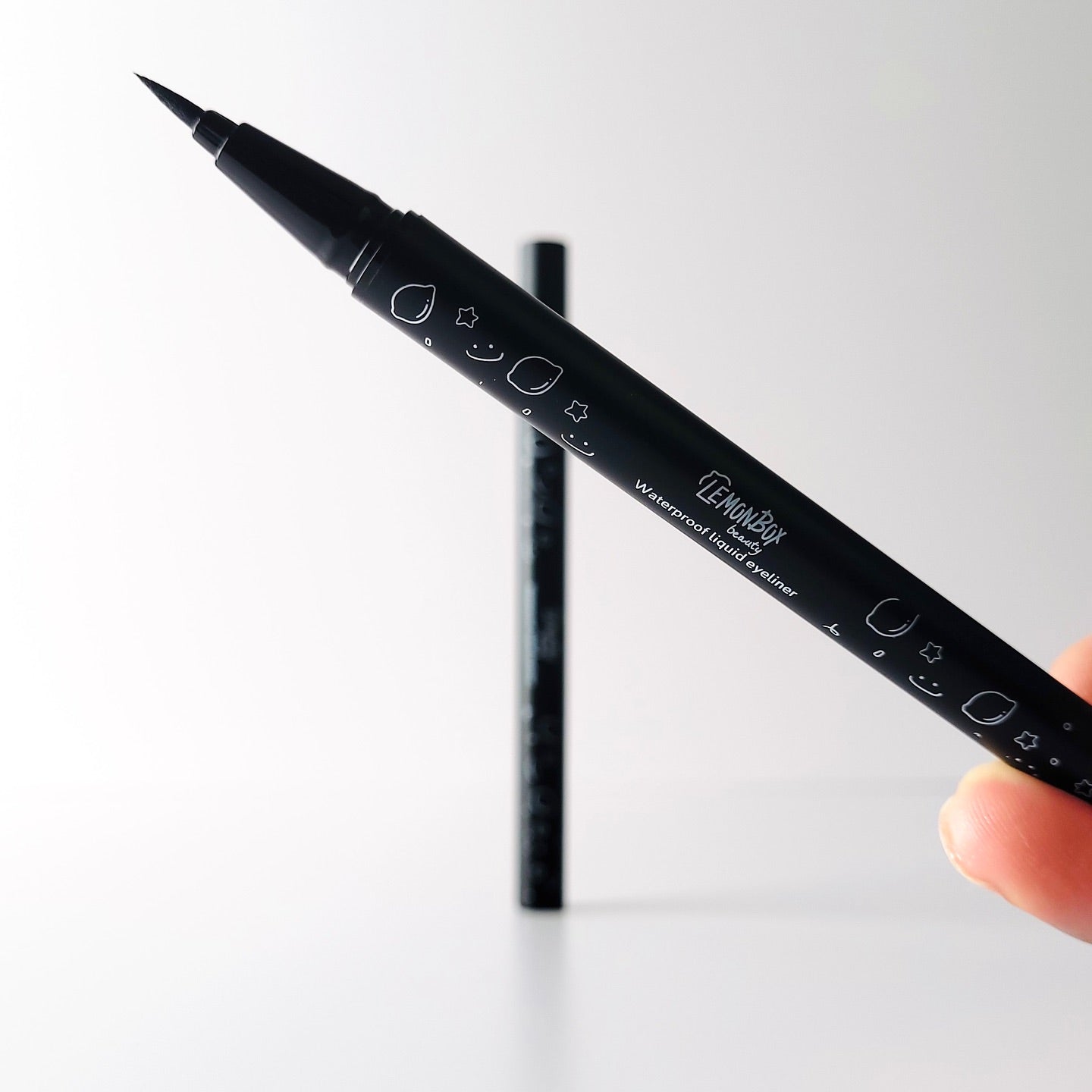 Black marker Felt tip eyeliner pen held by a hand on a white background