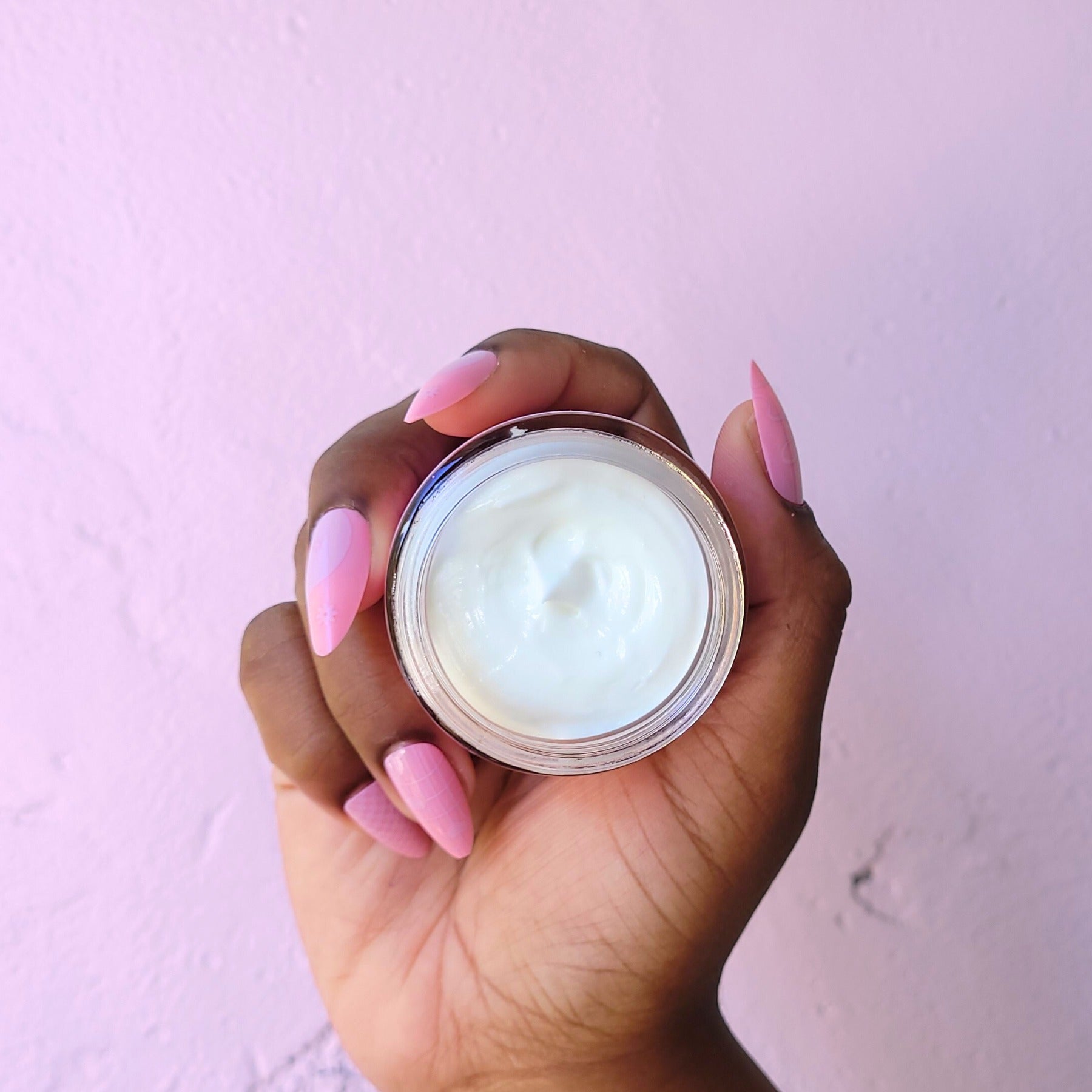 Hand holding a jar of cream against a light pink background Cherry Blossom