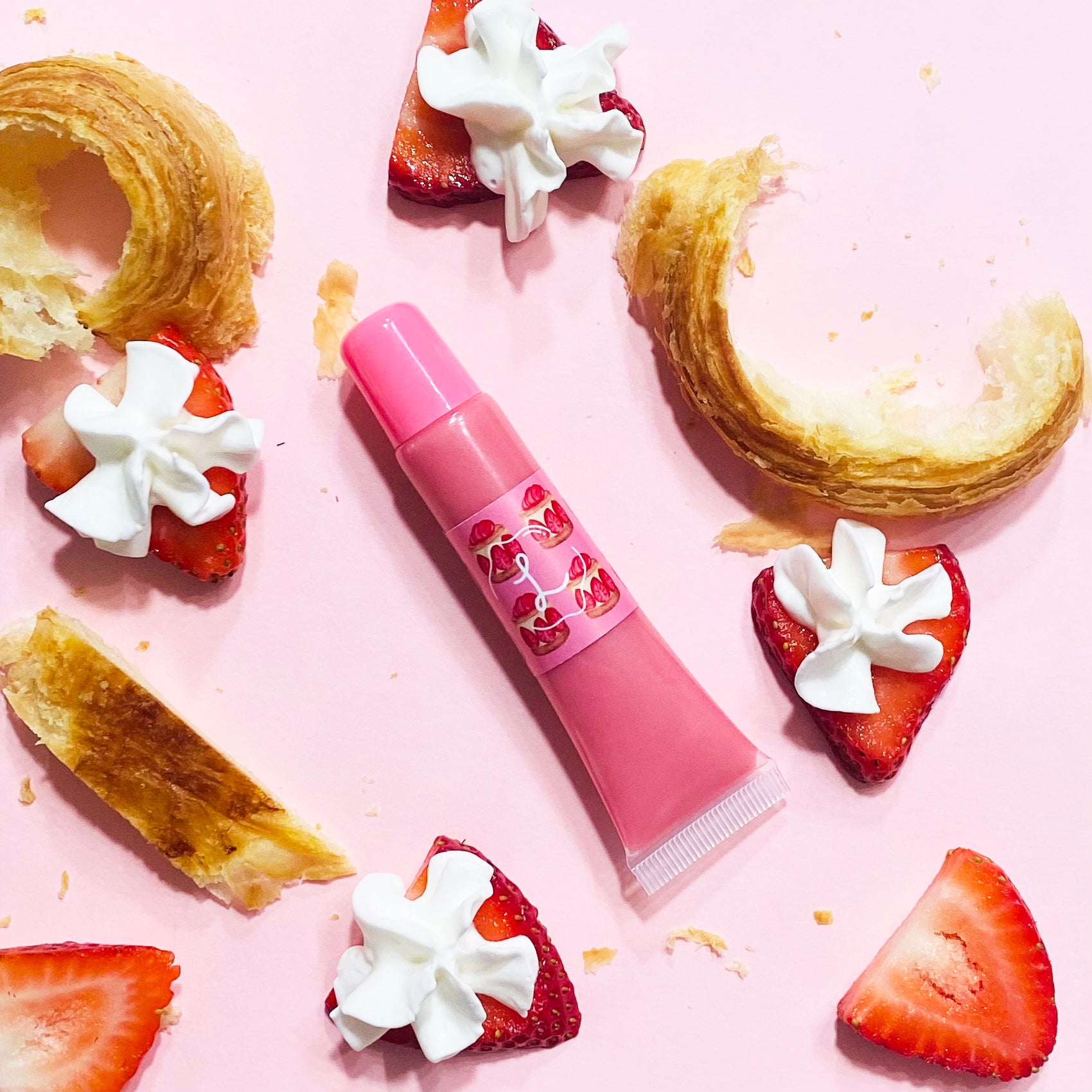 Pink lip balm with strawberry design on a pink background with strawberries and pastries.