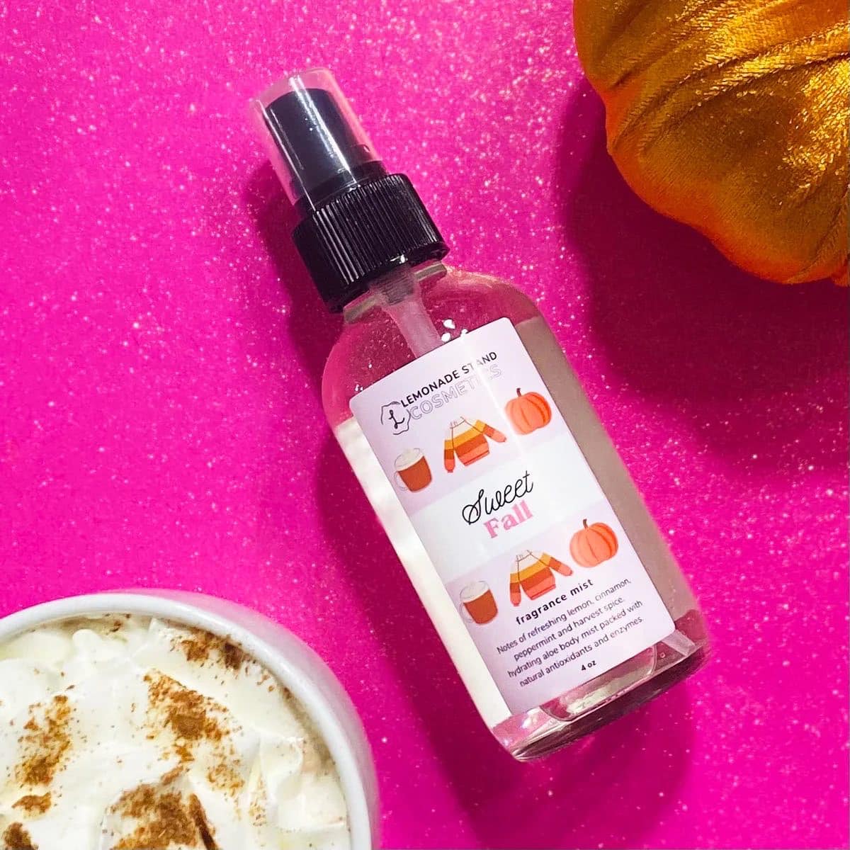Bottle of 'Sweet Fall' fragrance mist on a pink background with a bowl of latte and pumpkin.