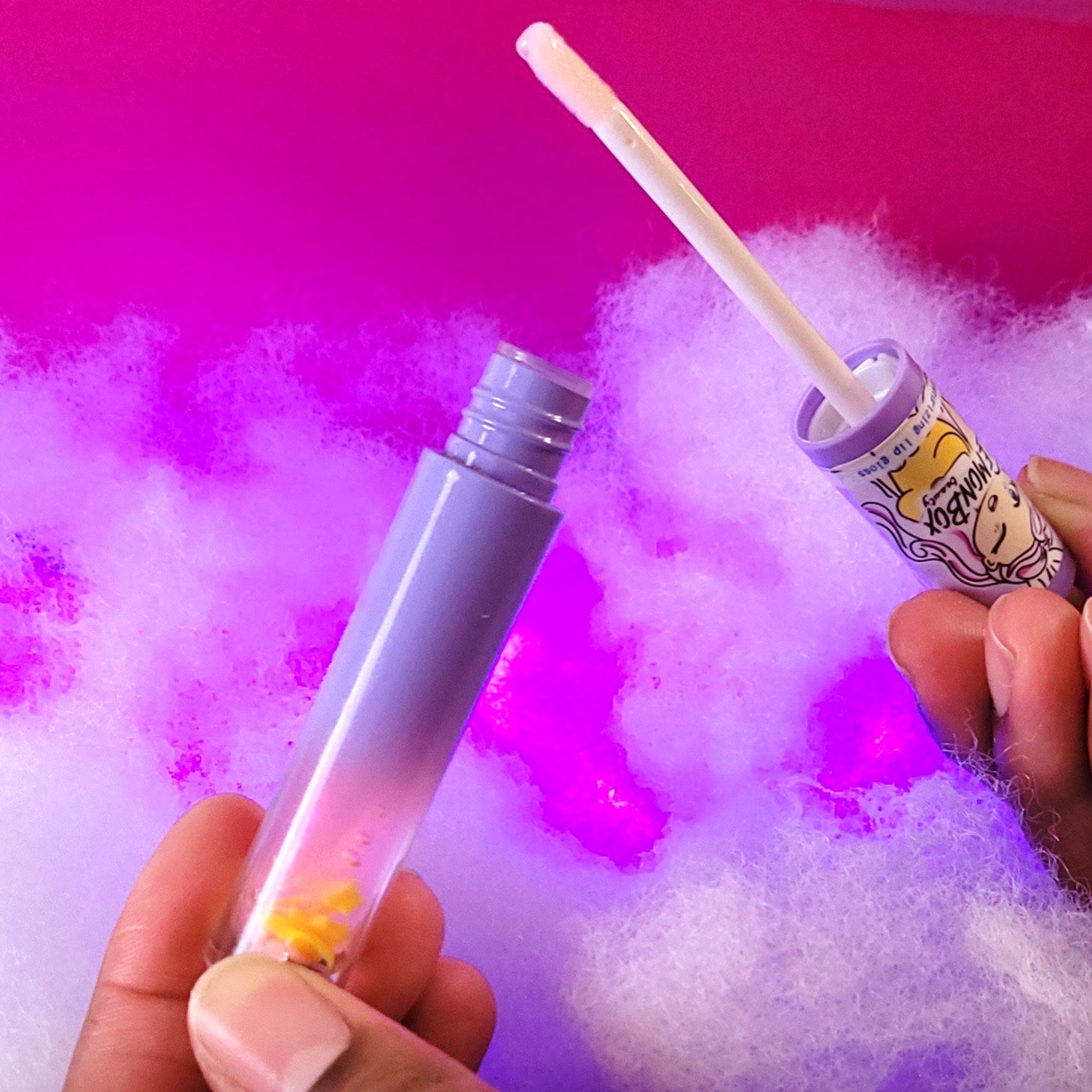 Two lip gloss products held against a colorful, textured background