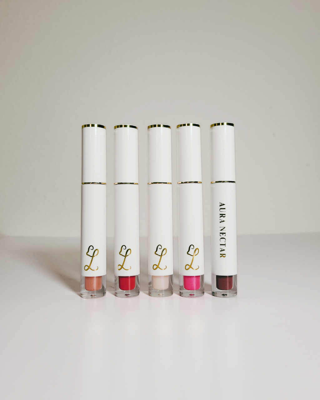 Five Alera Nectar lip gloss tubes in various shades, arranged in a row on a clean white surface against a light gray background.