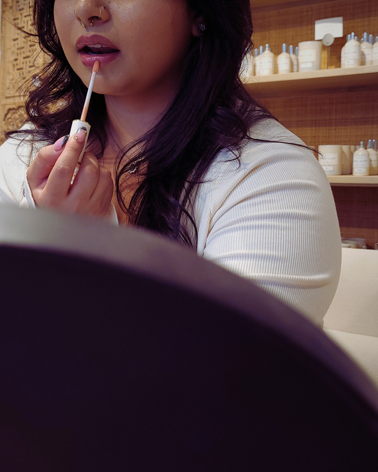 Woman applying lipstick in a setting with shelves in the background