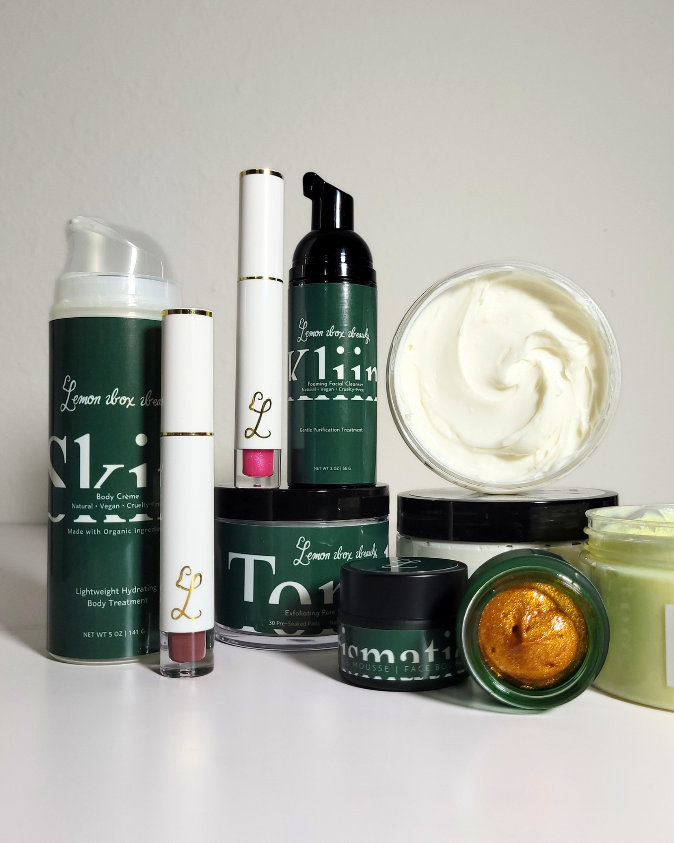 A collection of body care products from Lemon Shower, including a body powder canister, a lip gloss tube, a pump bottle, a whipped cream tub, and other jars, arranged on a white surface against a light gray background.
