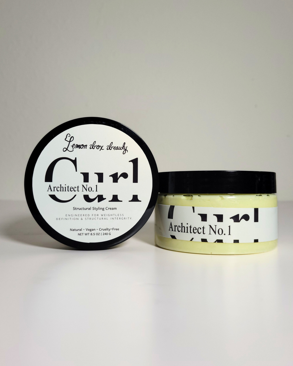 A jar of Architect No. 1 Structured Styling Cream next to its lid, which displays 'Lemon Thru Cream' in script and bold text.
