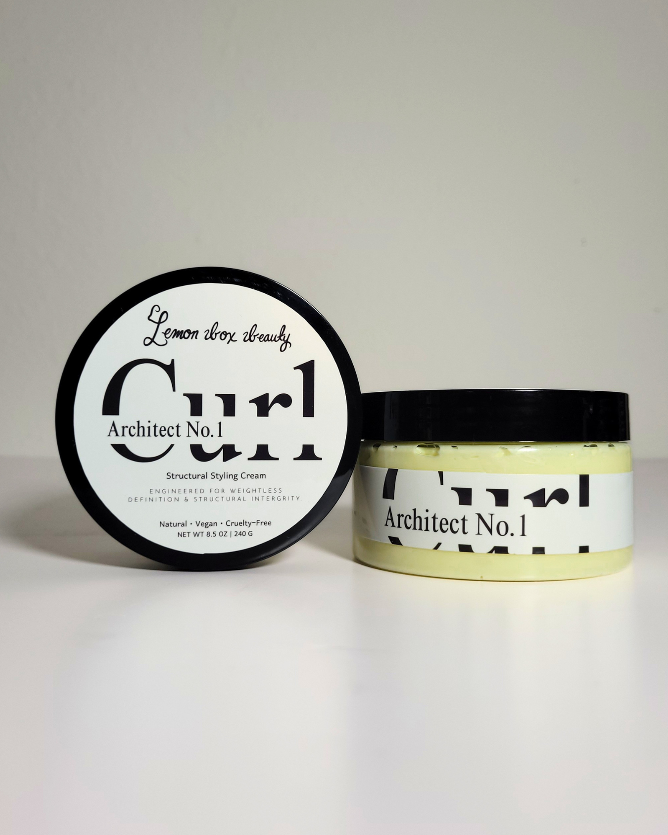 A jar of Architect No. 1 Structured Styling Cream next to its lid, which displays 'Lemon Thru Cream' in script and bold text.