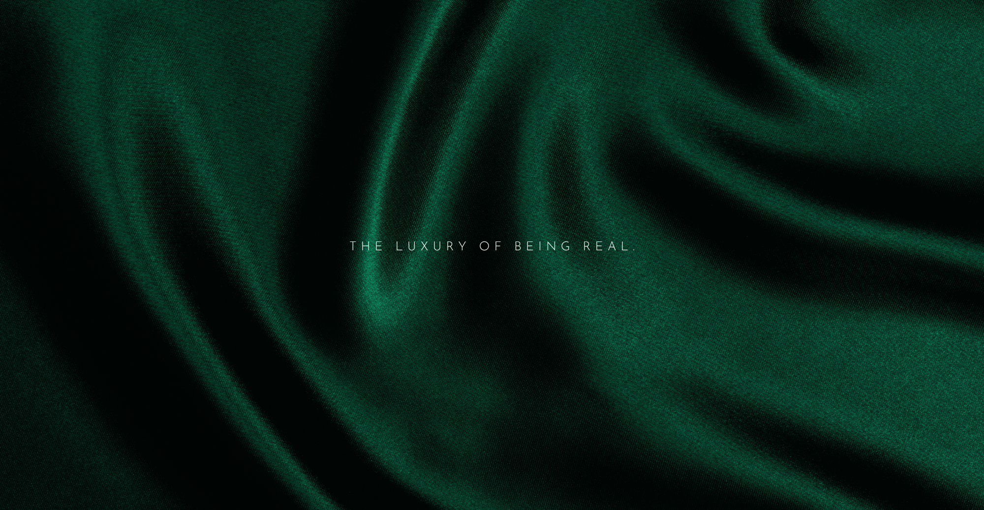 Dark green fabric texture with a subtle wave pattern and text 'THE LUXURY OF BEING REAL' on a dark background.
