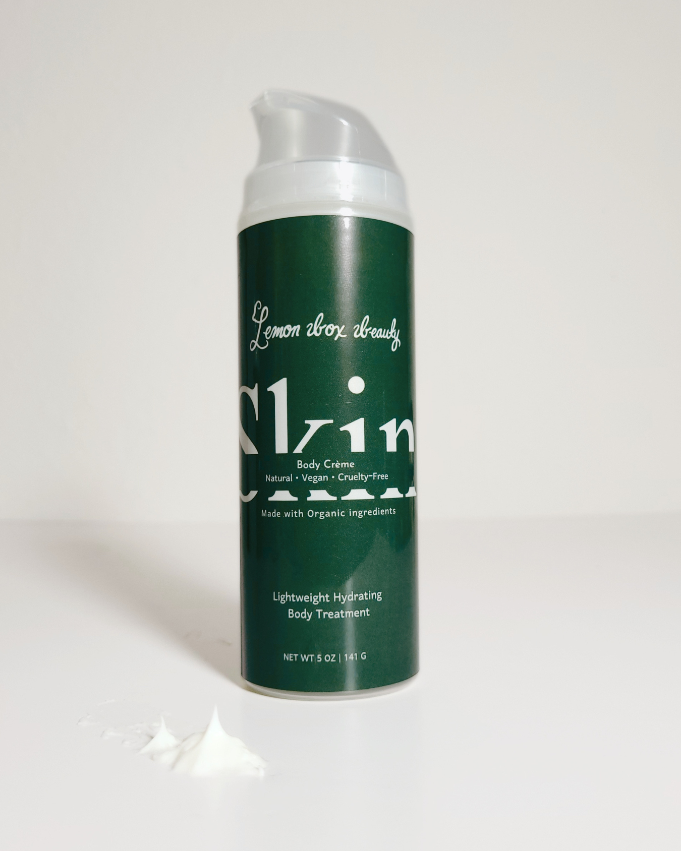 A dark green pump bottle of Alzin Lemon Drop Body Butter with white text, shown on a light gray background with a dollop of white cream in the foreground.